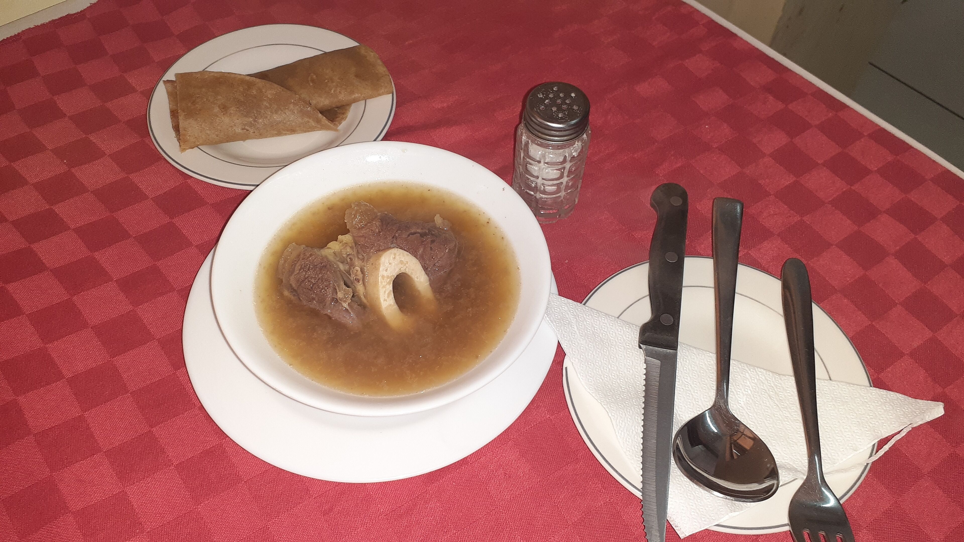 A table with a bowl of soup, two plates with food, and cutlery.