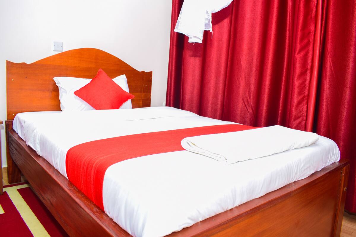 A neatly made bed with white and red bedding, a wooden headboard, and red curtains.