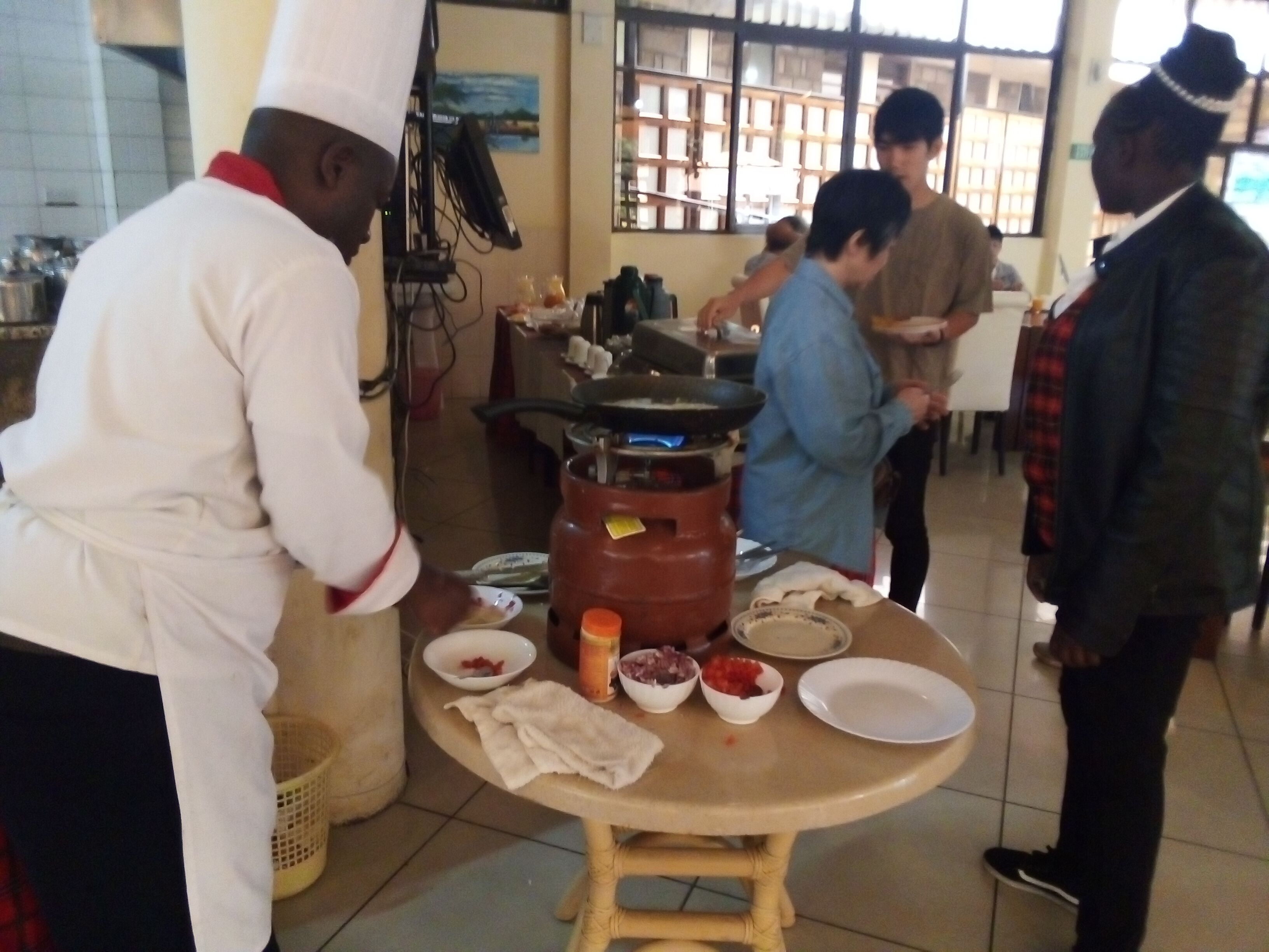 Una cuina amb una olla gran, diversos recipients d'ingredients i una persona preparant menjar.