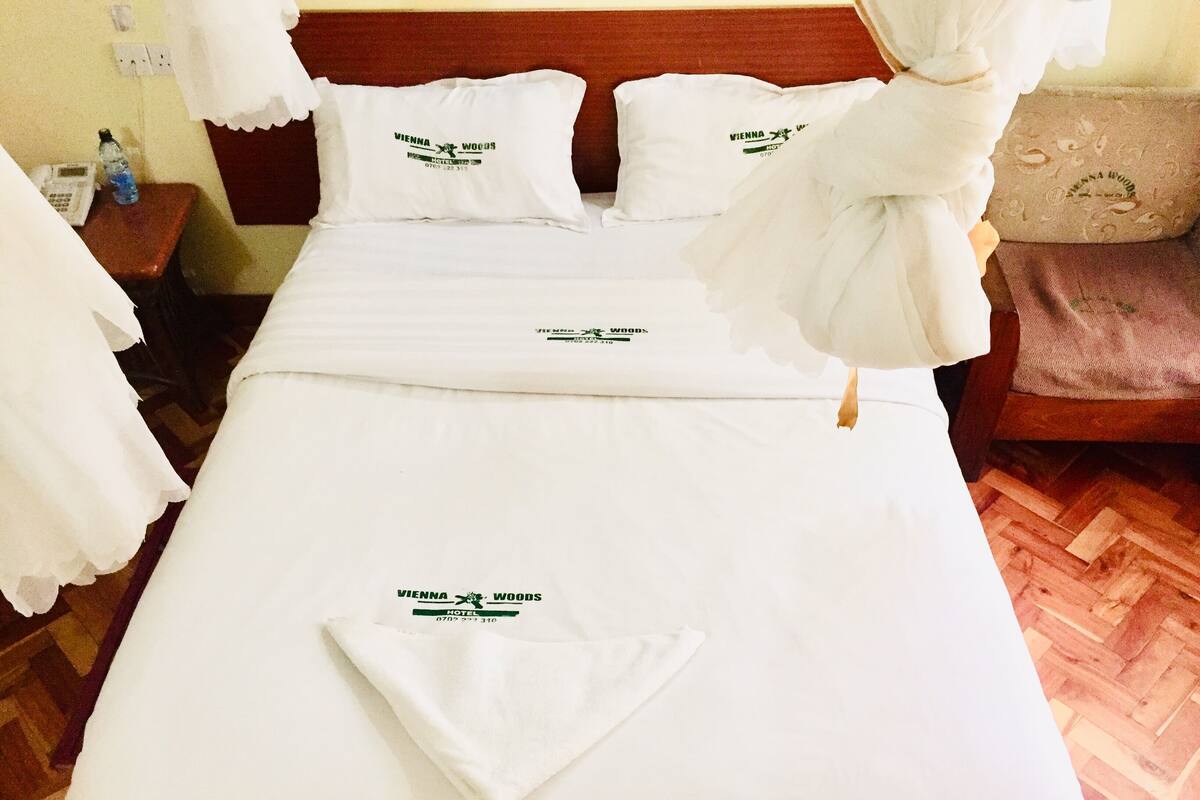 A hotel room with a neatly made bed, white bedding, and a towel on the bed.