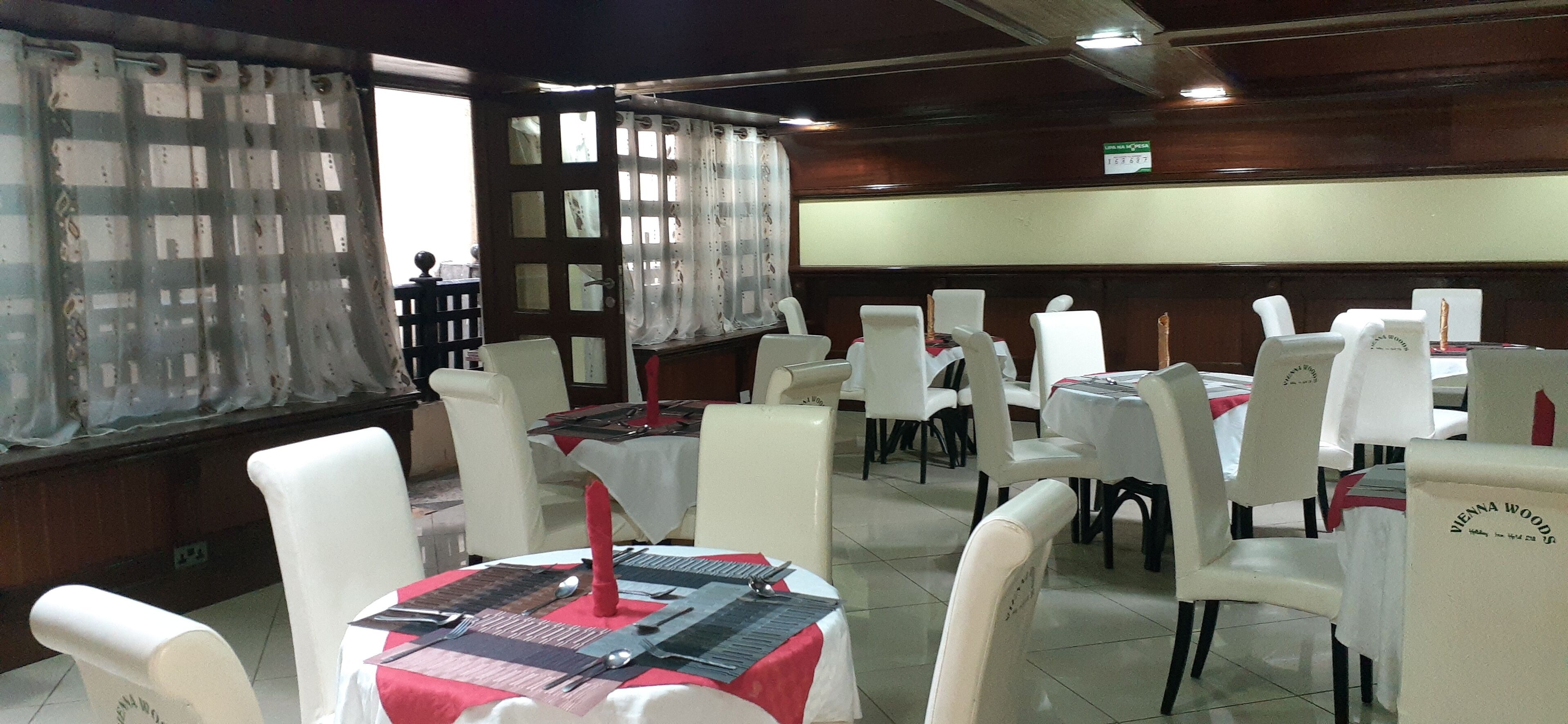 A restaurant with white chairs and tables, some with red tablecloths.