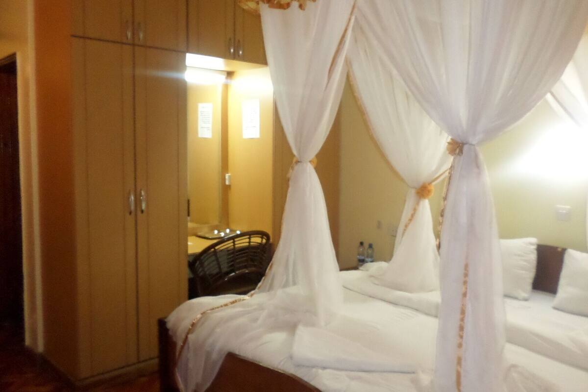 A hotel room with a canopy bed, a wardrobe, and a mirror.