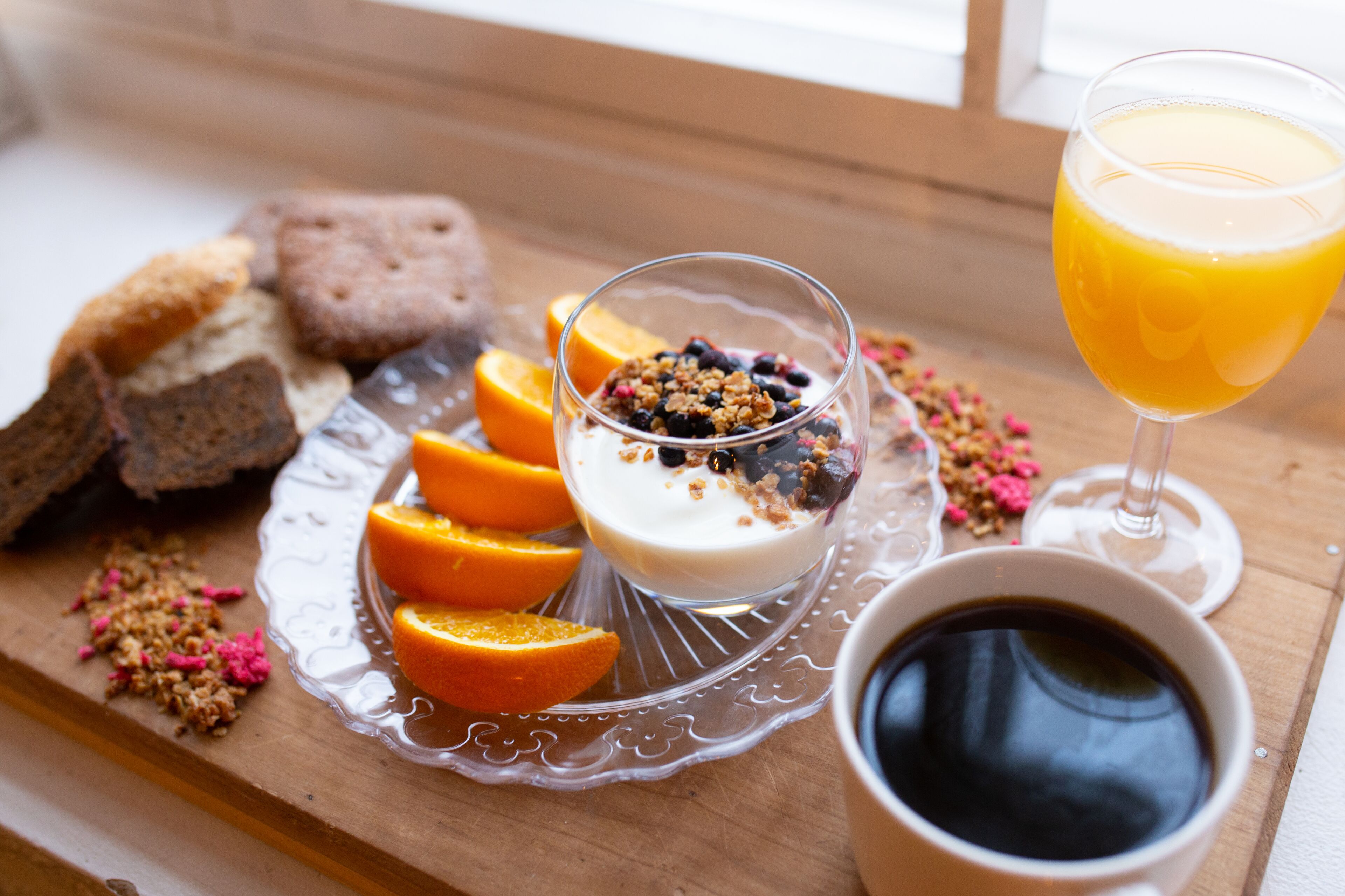 Ein Frühstücksbrett mit Joghurt, belegt mit Granola und Beeren, Orangenscheiben und einem Glas Orangensaft.