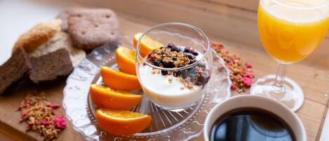 Ein Frühstücksbrett mit Joghurt, belegt mit Granola und Beeren, Orangenscheiben und einem Glas Orangensaft.