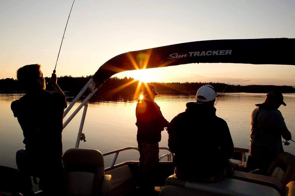 Veneessä on «Sun Tracker» -merkkinen kyltti, sen kannella on ihmisiä ja taustalla auringonlasku veden yllä.