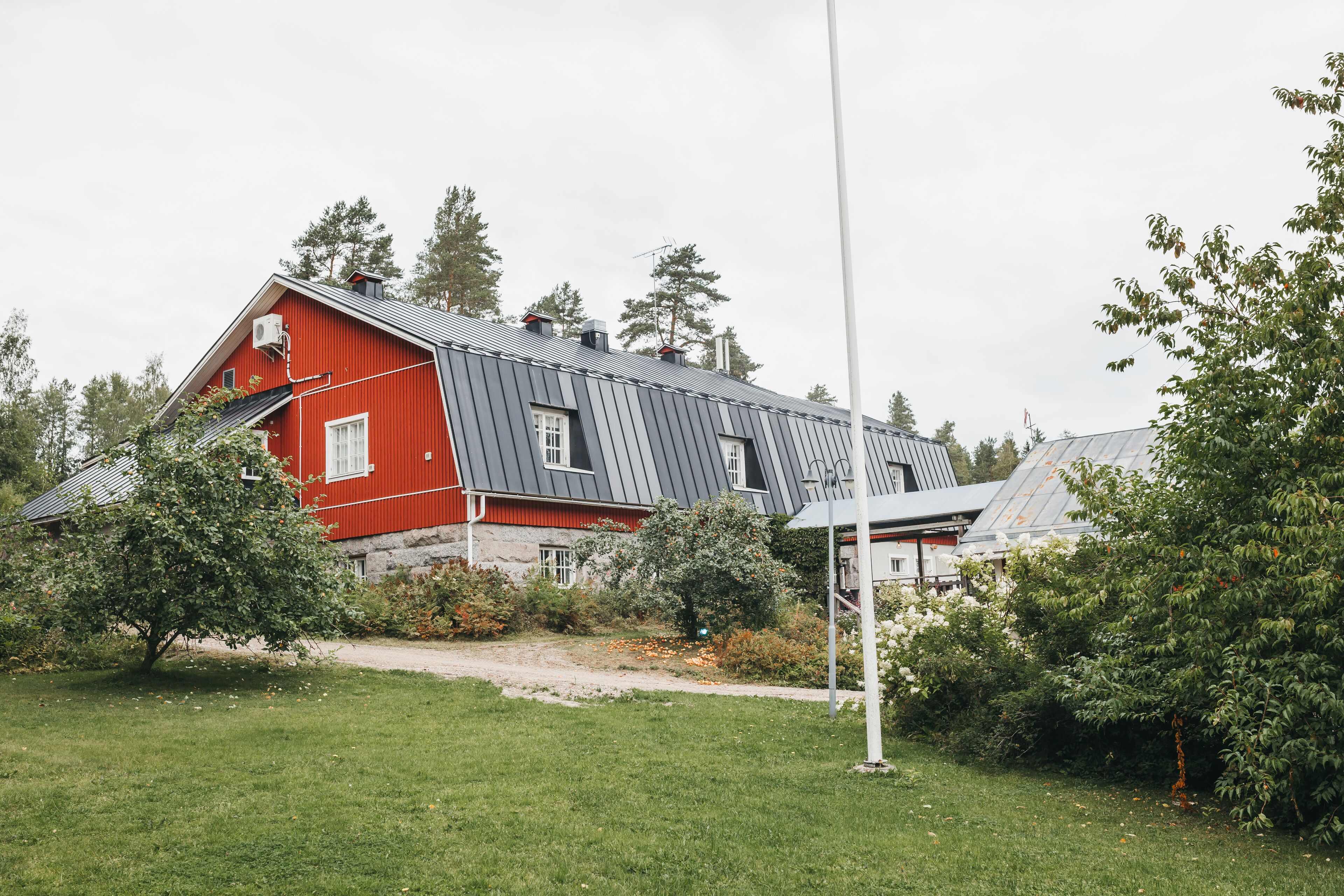 Ein rotes und graues Haus mit einem Metall-Dach, umgeben von Grünflächen und Bäumen.