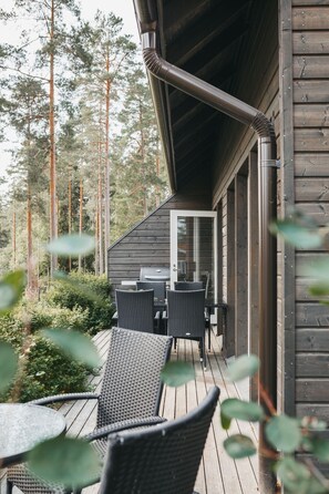 A wooden deck with wicker furniture and a grill, surrounded by tall trees.