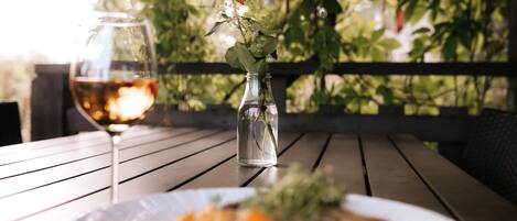 Uma mesa de jantar com um prato de comida, um copo de vinho e um pequeno vaso com uma rosa.