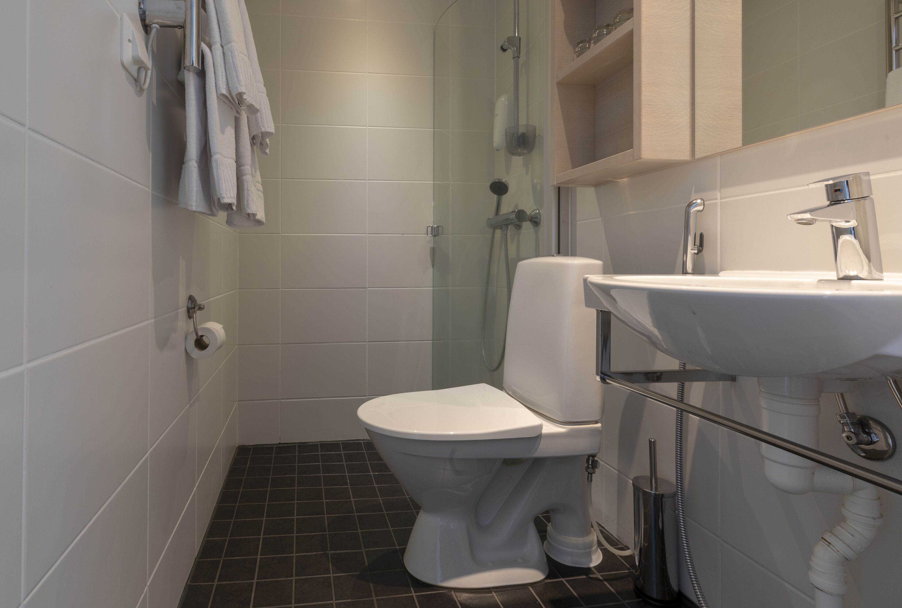 Ein Badezimmer mit Toilette, einer Glasdusche, einem Waschbecken mit Spiegel und einem Handtuchhalter.