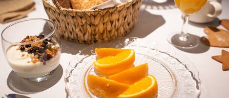 A breakfast setting with a plate of orange slices, a bowl of yogurt with granola, a glass of orange juice, and a basket of bread.