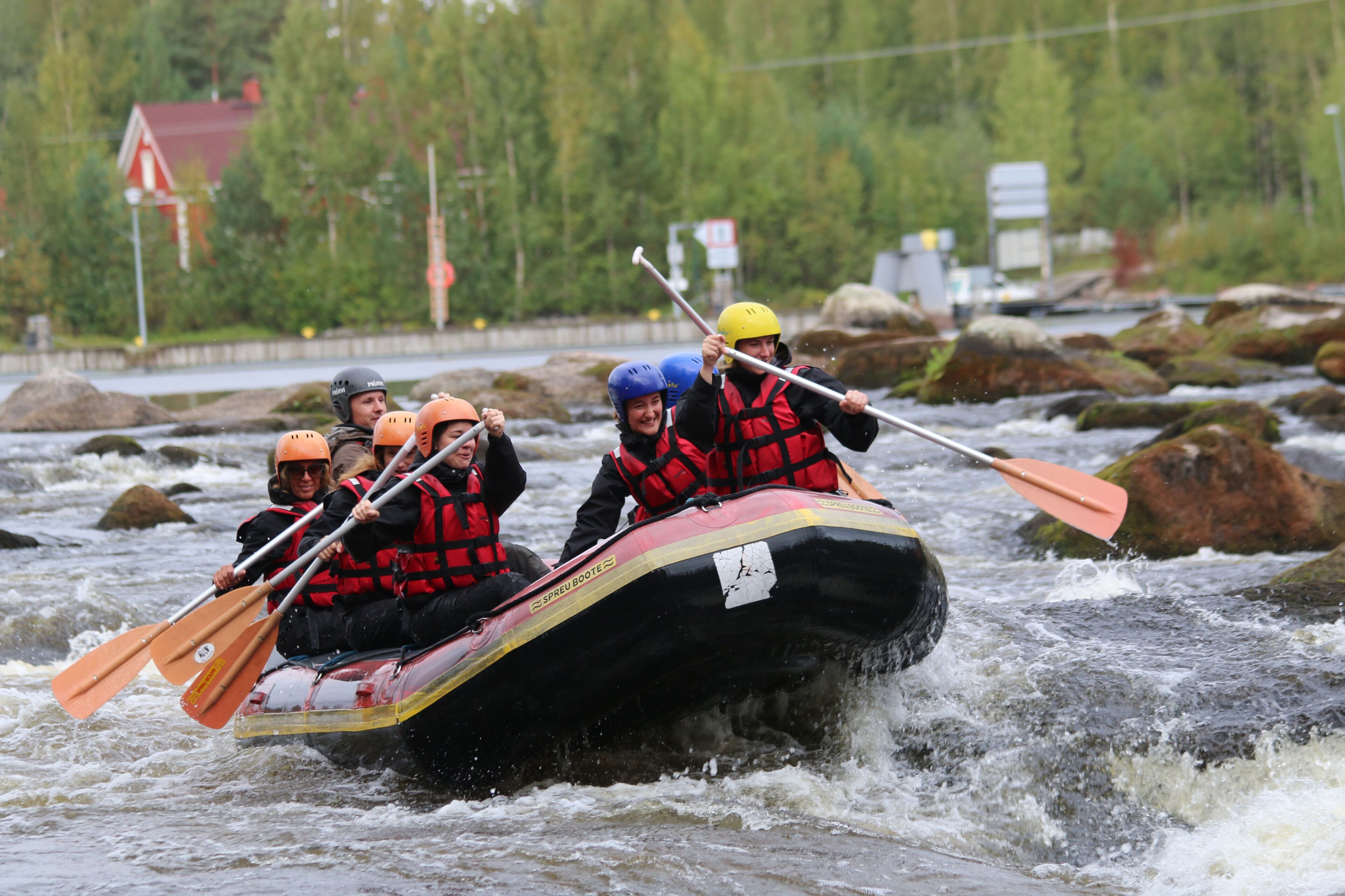 Een groep mensen peddelt in een raft over een rivier vol rotsen.