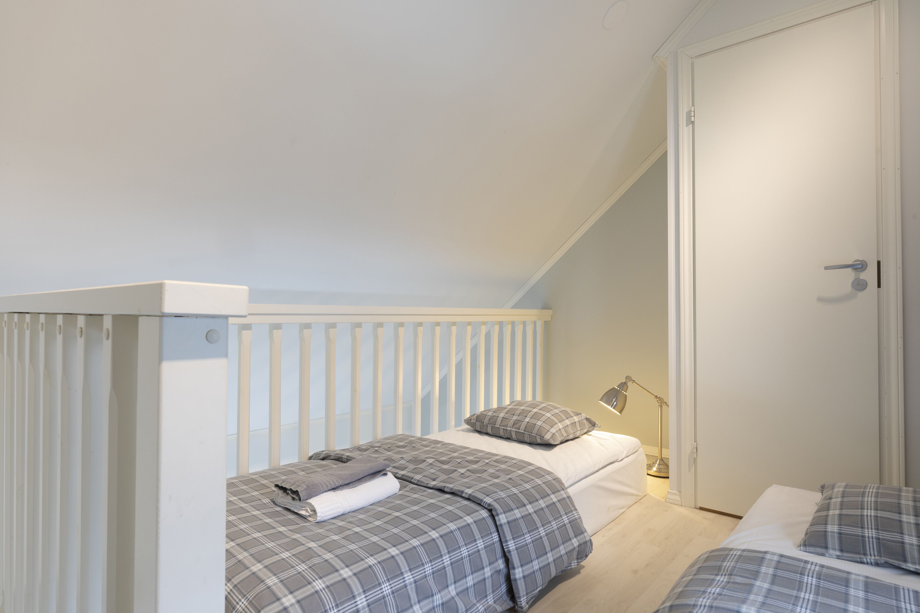A bedroom with a bunk bed, a bedside table with a lamp, and a door.