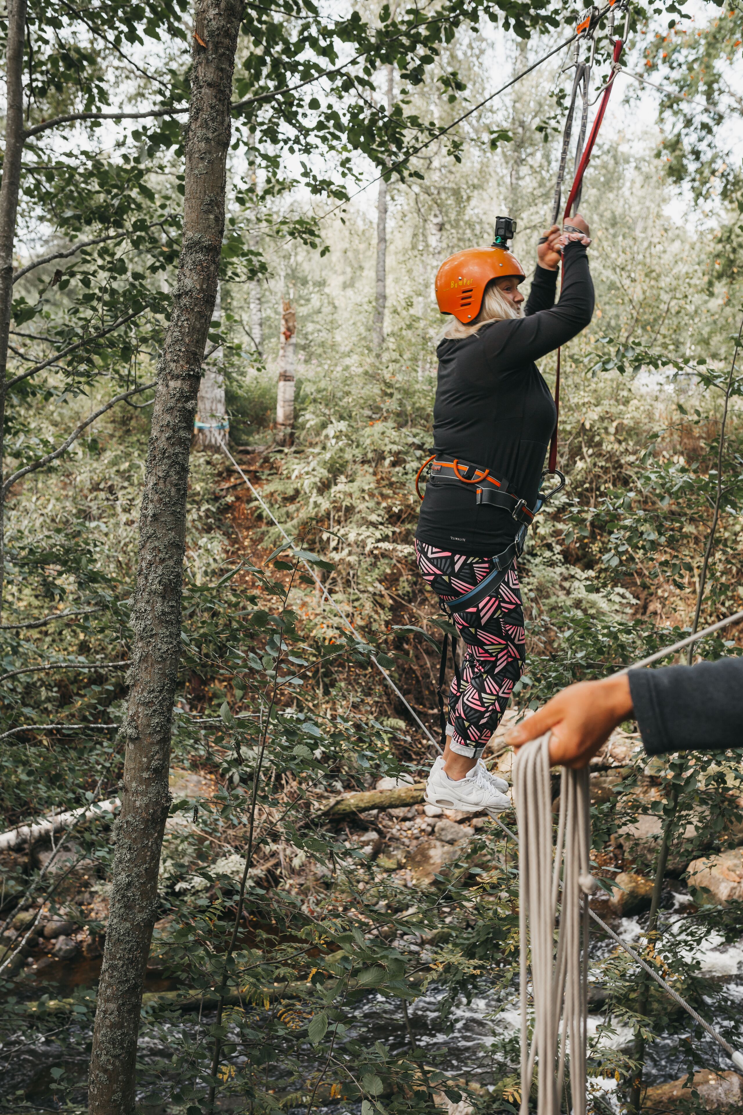 A person in a forested area with a rope and harness, indicating outdoor adventure activities.