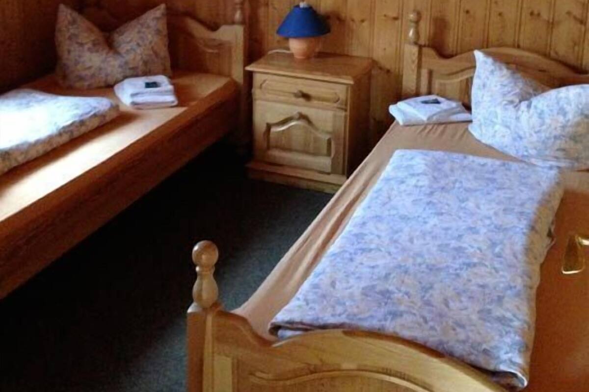 Quarto de madeira com duas camas de solteiro, mesa de cabeceira com abajur e uma pequena mesa.