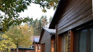 Eine Holzhütte mit einer Terrassenfläche, einem kleinen Tisch und Stühlen sowie einem gepflasterten Weg.