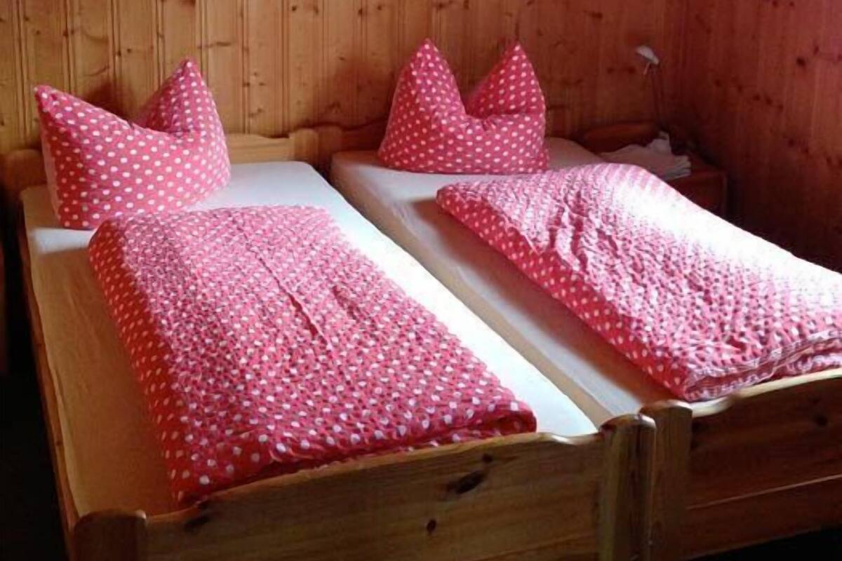Um quarto com painéis de madeira e duas camas de solteiro, cada uma com um edredom e almofadas estampadas em bolinhas rosa.