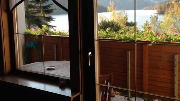 Ein Zimmer mit großem Fenster, Blick auf Garten und See.