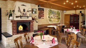 Ein Restaurant mit Backsteinofen, Holzbalkendecke und gedeckten Tischen für Gäste.