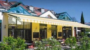 A building with a yellow awning and a glass roof, surrounded by greenery. - Hotel beim Hirschen (Merzhausen)