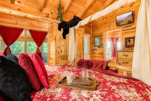 Quarto acolhedor de cabana de tronco com uma cama, uma televisão e uma janela com cortinas.