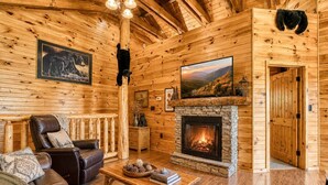 A log cabin interior with a fireplace, leather seating, wooden walls, and a mounted bear. - Bear Elegance  - Theater Room, Secluded, Heart Shaped Tub!!! (Sevierville)
