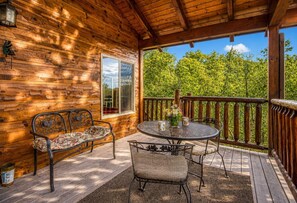 A wooden deck with a metal table and chairs, a bench, and a window overlooking greenery. - Bear Elegance  - Theater Room, Secluded, Heart Shaped Tub!!! (Sevierville)