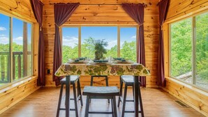 A wooden cabin with a dining table set for four, large windows, and a view of greenery. - Bear Elegance  - Theater Room, Secluded, Heart Shaped Tub!!! (Sevierville)