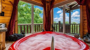 A wooden cabin with a hot tub, large windows, and a balcony with bear figurines. - Bear Elegance  - Theater Room, Secluded, Heart Shaped Tub!!! (Sevierville)