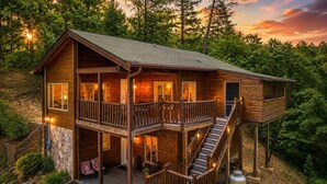 A two-story log cabin with a balcony, a staircase, and a stone foundation. - Bear Elegance  - Theater Room, Secluded, Heart Shaped Tub!!! (Sevierville)