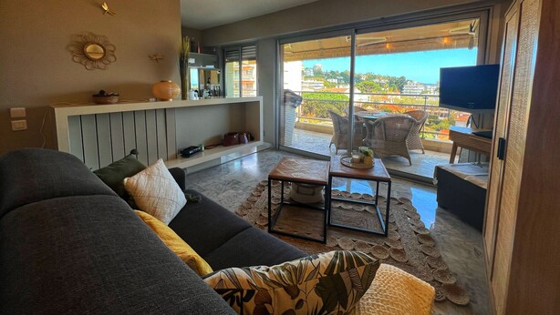 Ein modernes Wohnzimmer mit grauem Sofa, einem Couchtisch und einem Balkon mit Korbmöbeln.