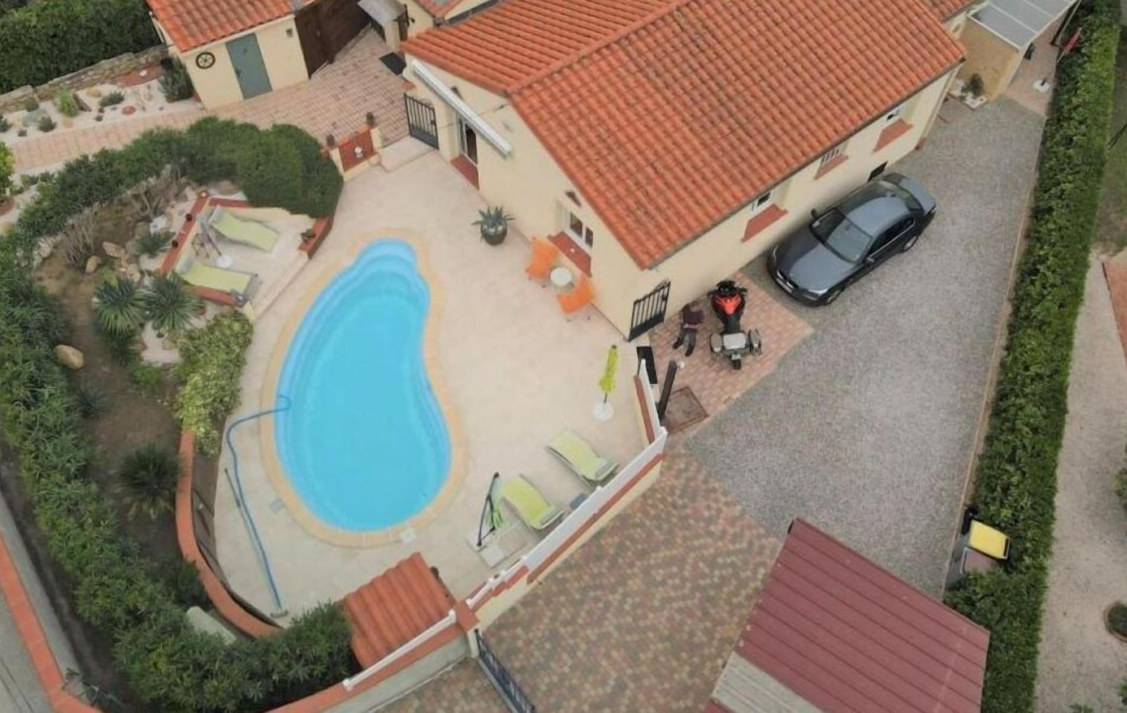 An aerial view of a house with a swimming pool, a car parked outside, and a red-tiled roof.