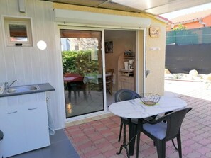 A kitchen with a sink and cabinets, a dining table with chairs, and a sliding glass door leading to an outdoor area. - La Picholine (Sorede)
