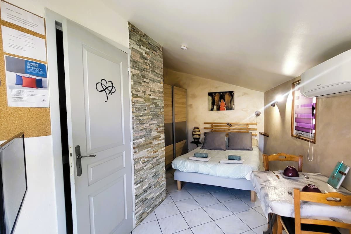 Une chambre à coucher comprenant un lit, un bureau, une chaise, une armoire et un tableau d’affichage en liège où sont accrochées des notes.