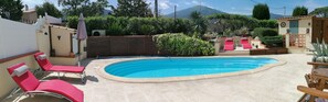 A swimming pool with red lounge chairs, a wooden deck, and a mountain view. - La Picholine (Sorede)