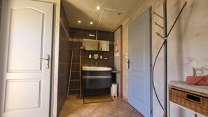A bathroom with a dark tiled wall, a white door, a sink, and a mirror. - La Picholine (Sorede)