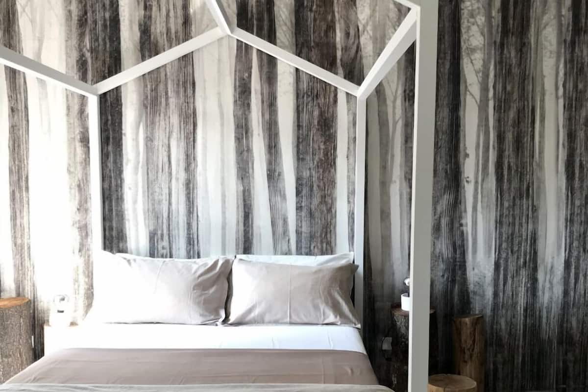 Un dormitorio moderno con una cama tipo dosel geométrica, un ventanal grande y una pared con textura.