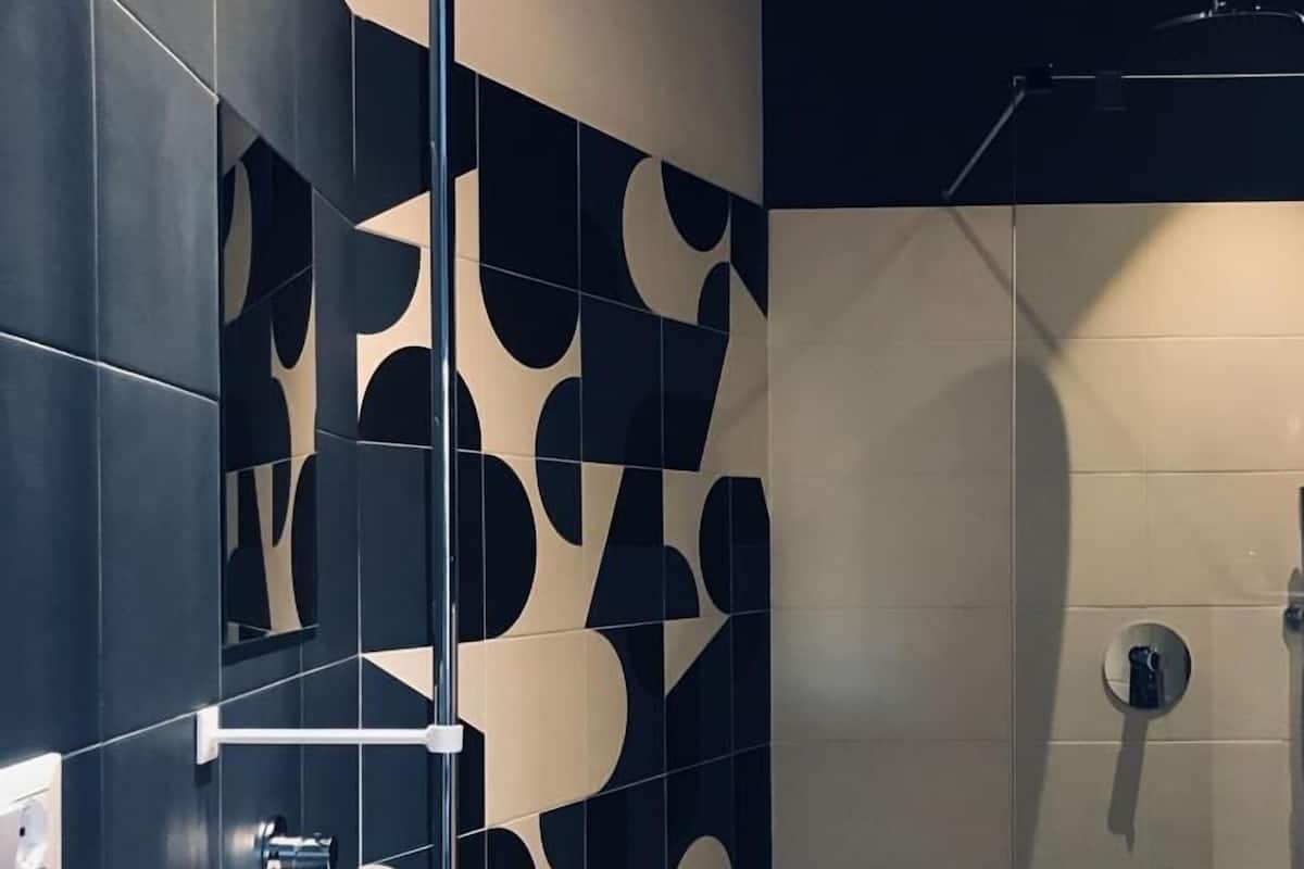 Un baño moderno con un lavamanos blanco, paredes de azulejos oscuros y una cabina de ducha de cristal.