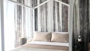 Una cama moderna con estructura geométrica, una colcha en tonos neutros y un fondo de papel tapiz con diseño de madera vertical.