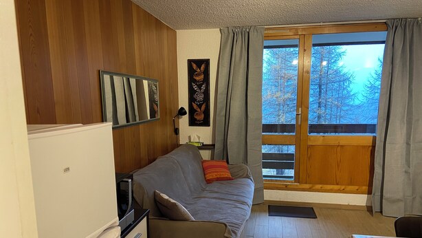 A compact living space with a kitchenette, a sofa, and a window with curtains.