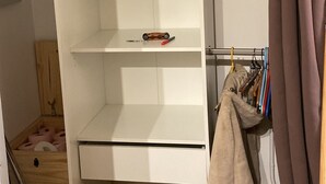 A partially open wardrobe with shelves and hanging space, a red bucket, and a wooden floor.
