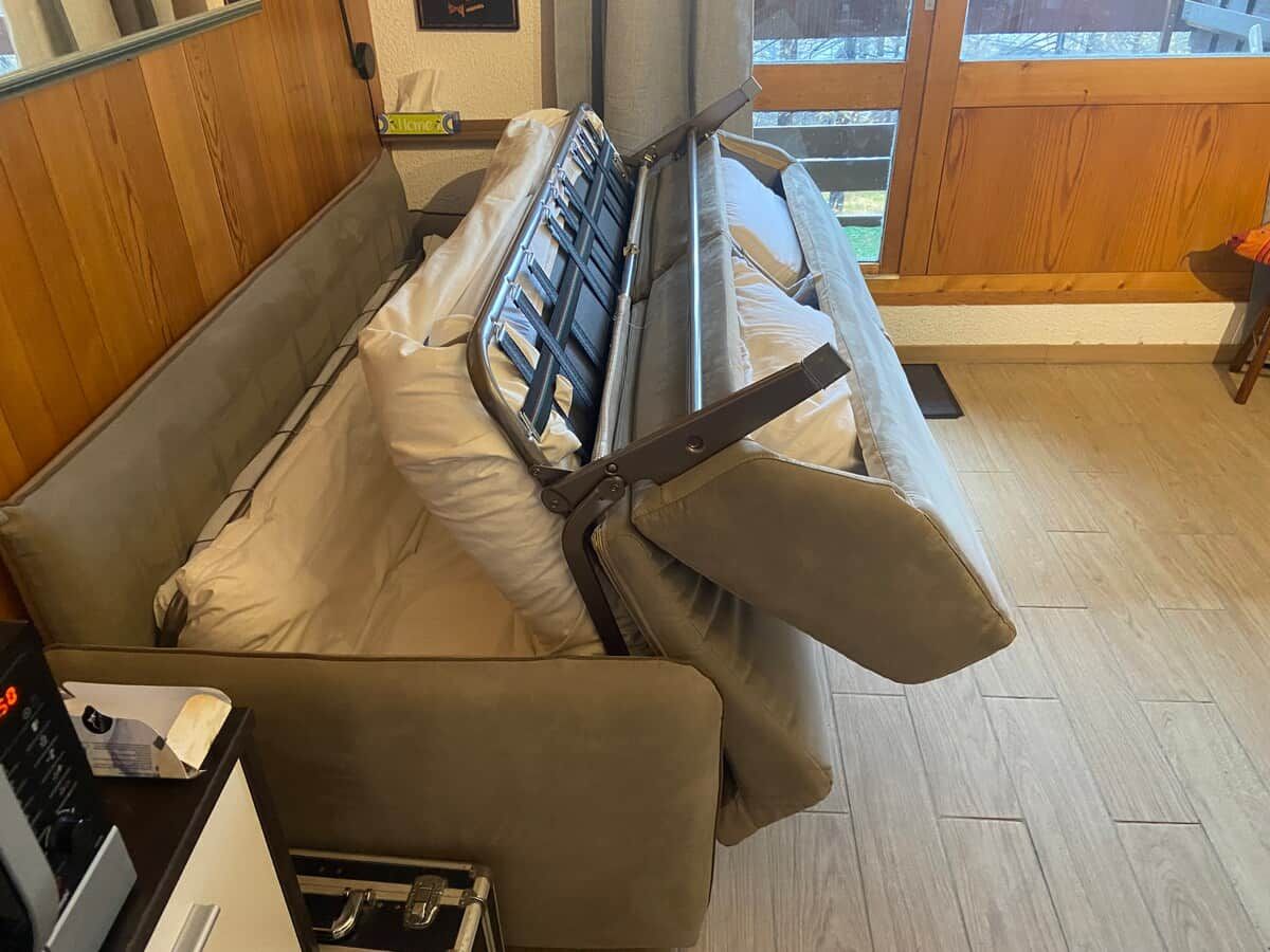 Een bed met hoofdeinde, een nachtkastje met een lamp en een raam met uitzicht op de omgeving.