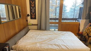 A bedroom with a bed, a desk, a chair, a window, and a view of trees.