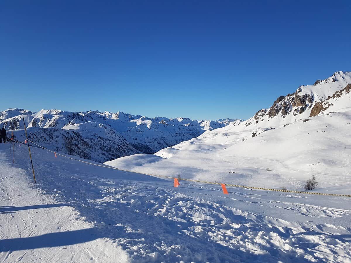 Een besneeuwd berglandschap met een piste, gemarkeerd met oranje stokken en een gele touw.