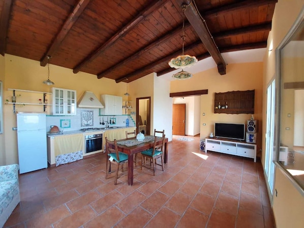 A spacious kitchen with a dining area, wooden ceiling beams, and a TV.