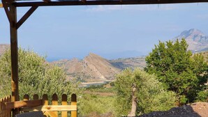Une pergola en bois, agrémentée de meubles en osier, offre une vue imprenable sur un paysage montagneux et la mer.