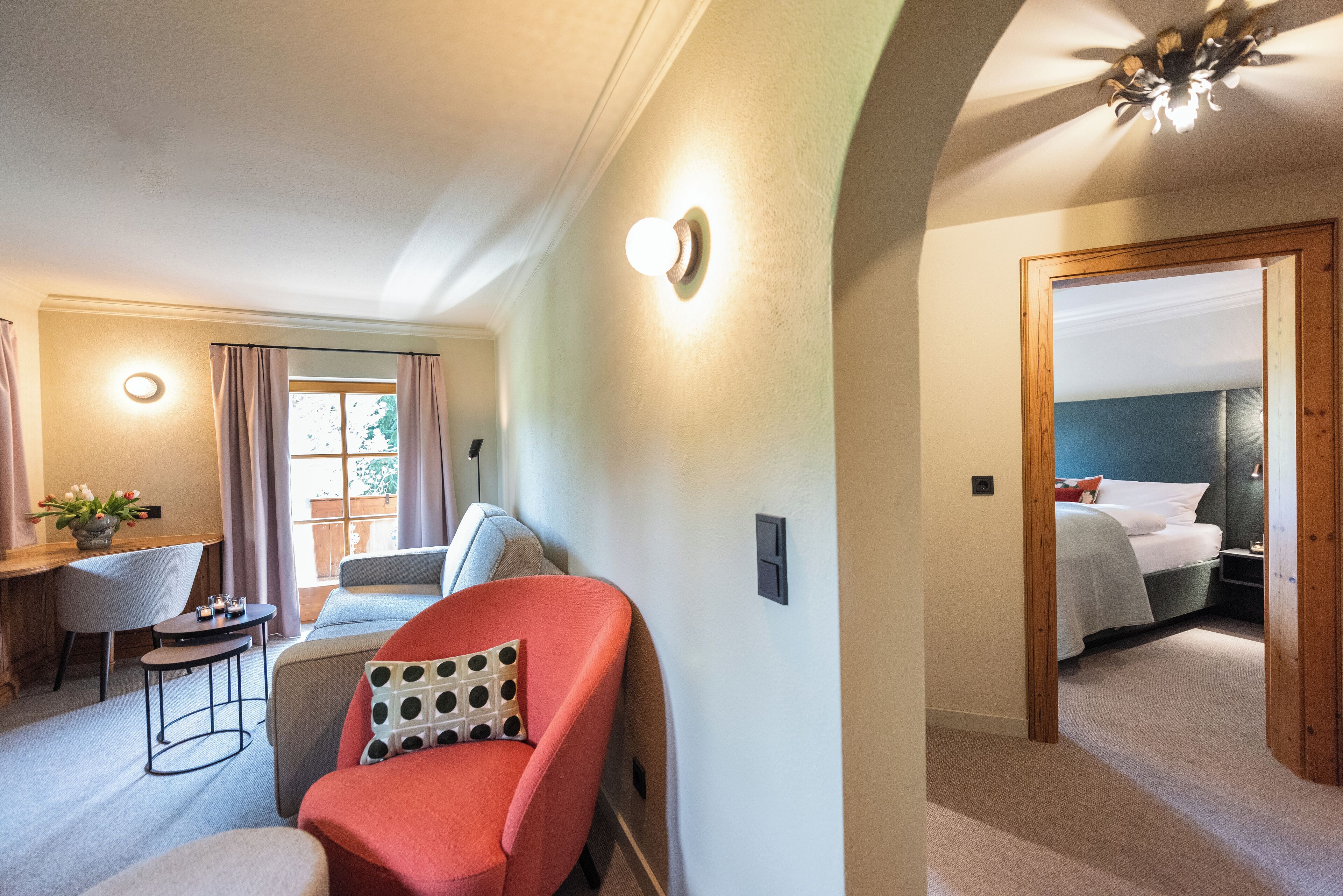 Una habitación de hotel con cama, escritorio, silla y una pequeña mesa con un jarrón de flores.