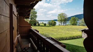A wooden balcony with a bench, overlooking a grassy field and a lake with trees and hills in the background. - Landhaus Christl am See (Bad Wiessee)