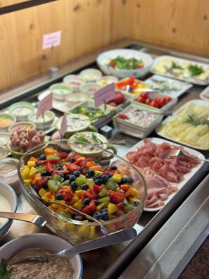 A buffet with various food options including a bowl of mixed fruit salad, meat platters, and other dishes. - Landhaus Christl am See (Bad Wiessee)