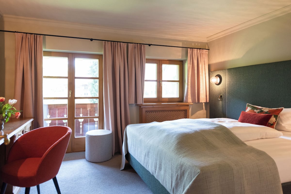 A hotel room with a bed, a chair, a small table, and a window with curtains.