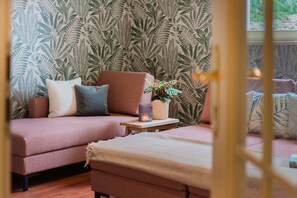 A cozy room with a patterned wallpaper, a sofa with cushions, a small table with a candle and a plant, and a bench. - Landhaus Christl am See (Bad Wiessee)